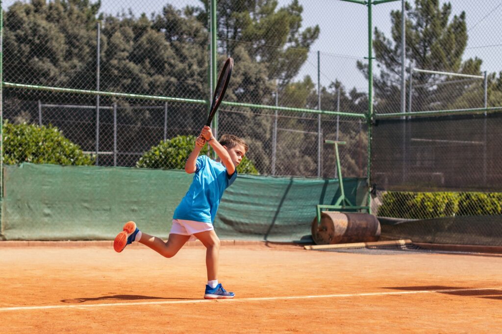 Little boy playing tennis on a dirt court