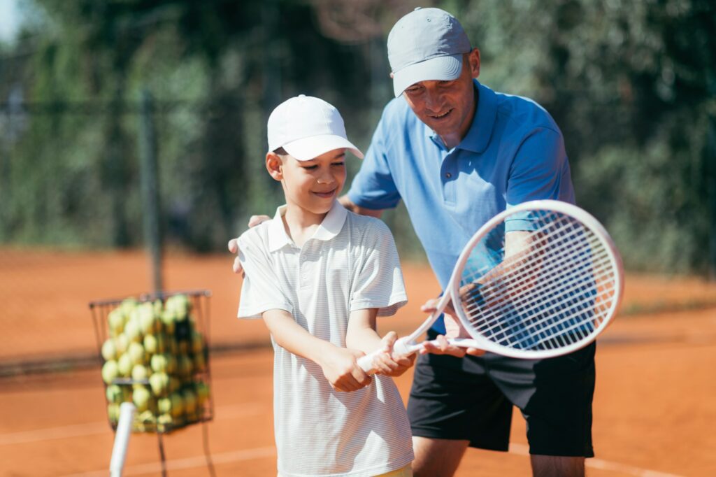 Tennis Lesson. Smiling Coach Explaining Tennis Technique to a Boy